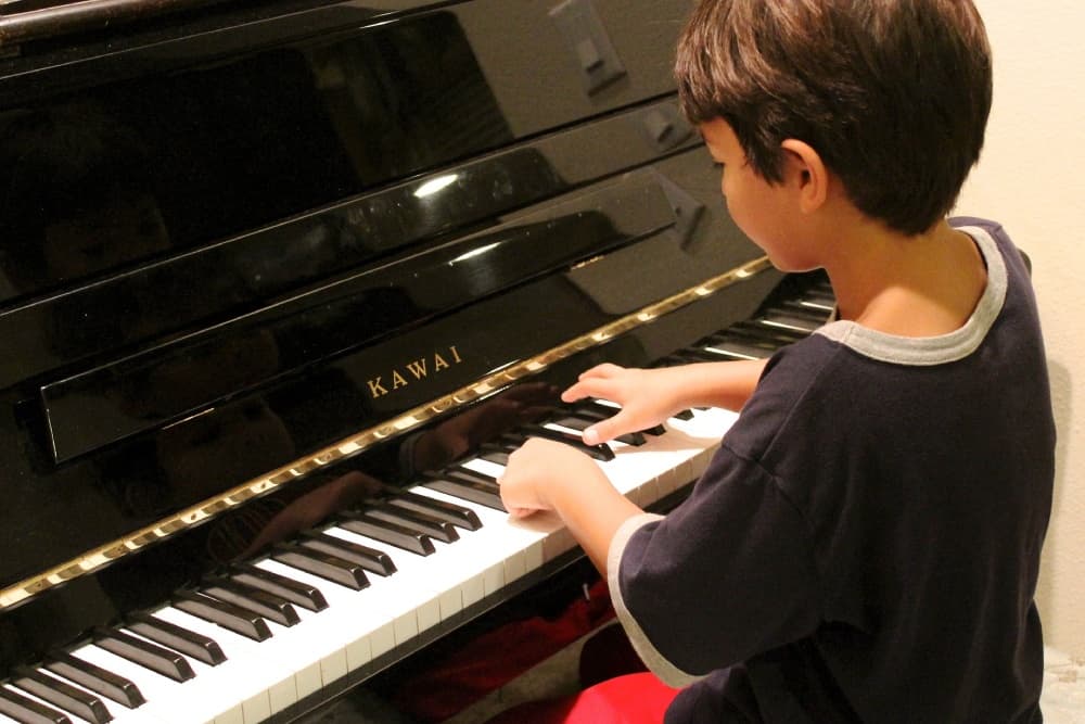 Young music student learning to play piano on a shiny black kawai piano