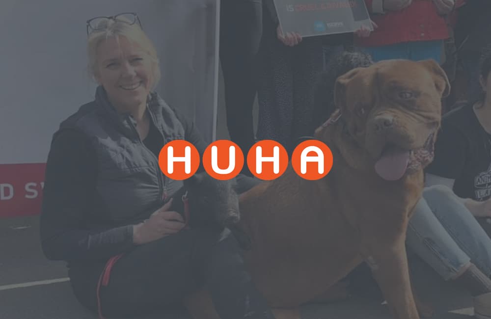 Happy Huha team member sitting with a little black piglet and a big ginger dog in her lap