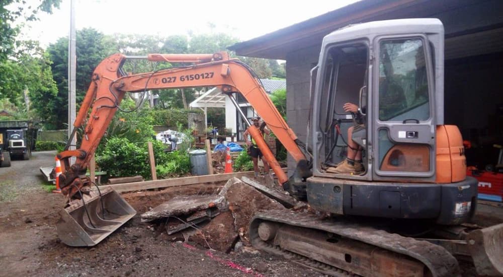 The ABC Excavation and landscaping team with a Vibrant orange digger excavating earth in a residential property's backyard