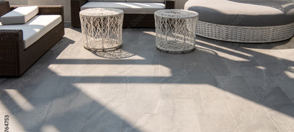 Outdoor seating area with a grey stone tile floor and white and dark grey outdoor furniture