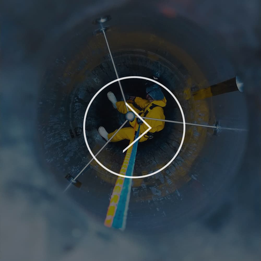 Abseiler rappelled down inside a tank to clean the interior while in a yellow jumpsuit, a hairnet, and a safety mask 