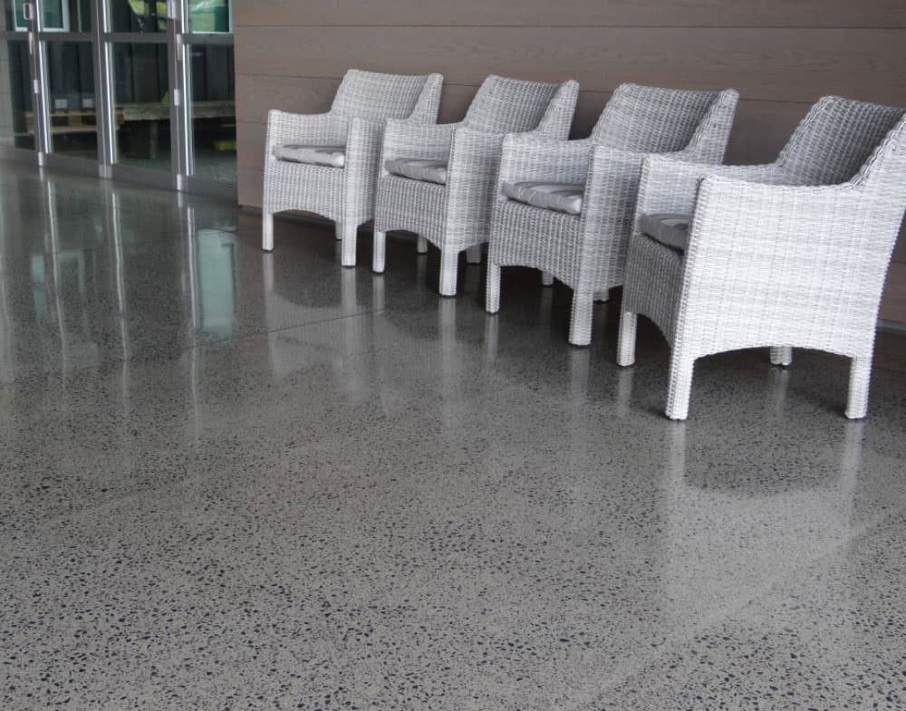 Shiny polished concrete floor outside a commercial building area with four white outdoor chairs
