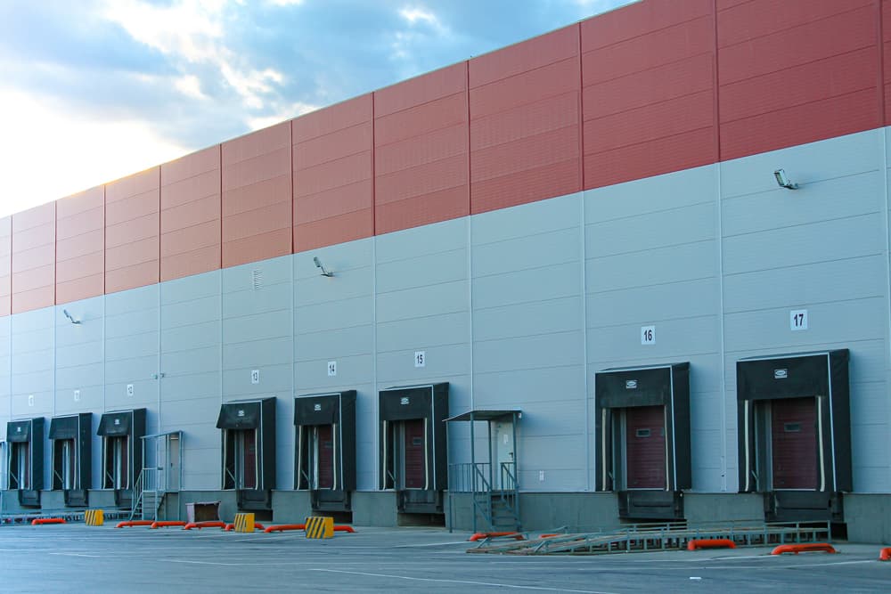 Large red and grey industrial warehouse with 7 truck loading bays with commercial garage doors and yellow barriers for safety