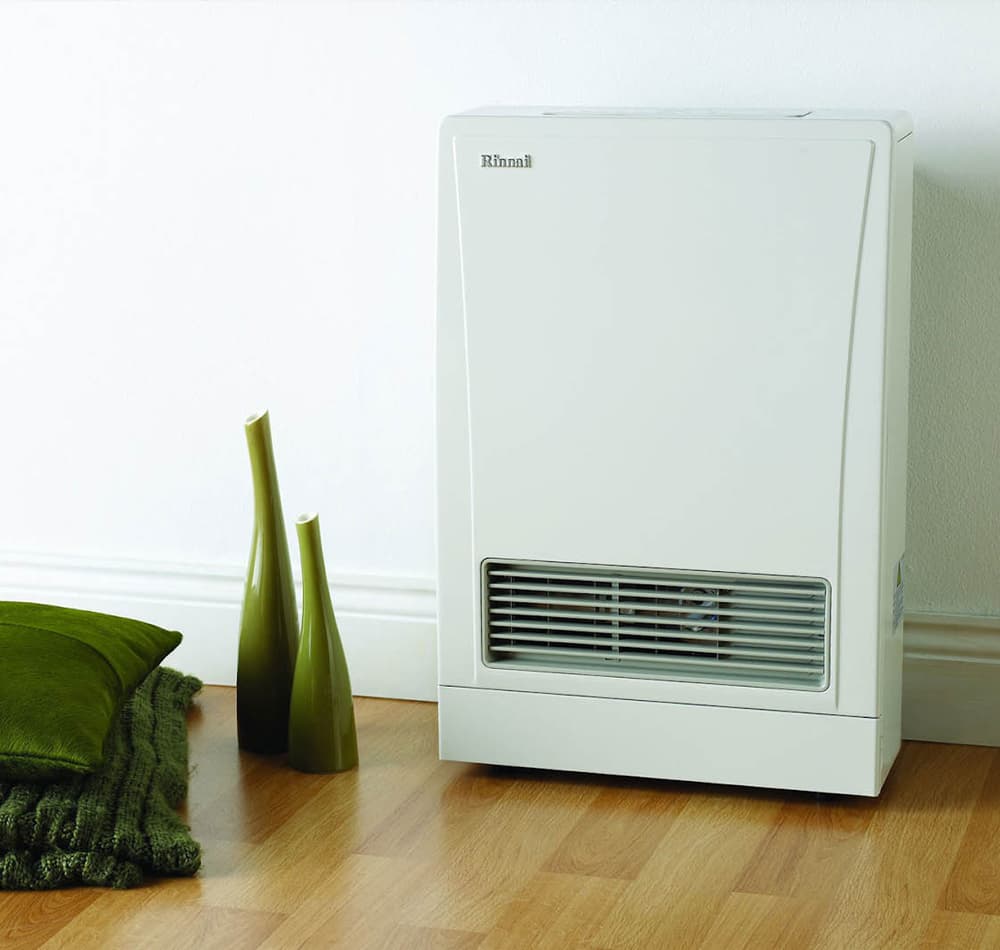 Wooden floor and a white wall with green ornaments and pillows next to a new white energysaver gas heater