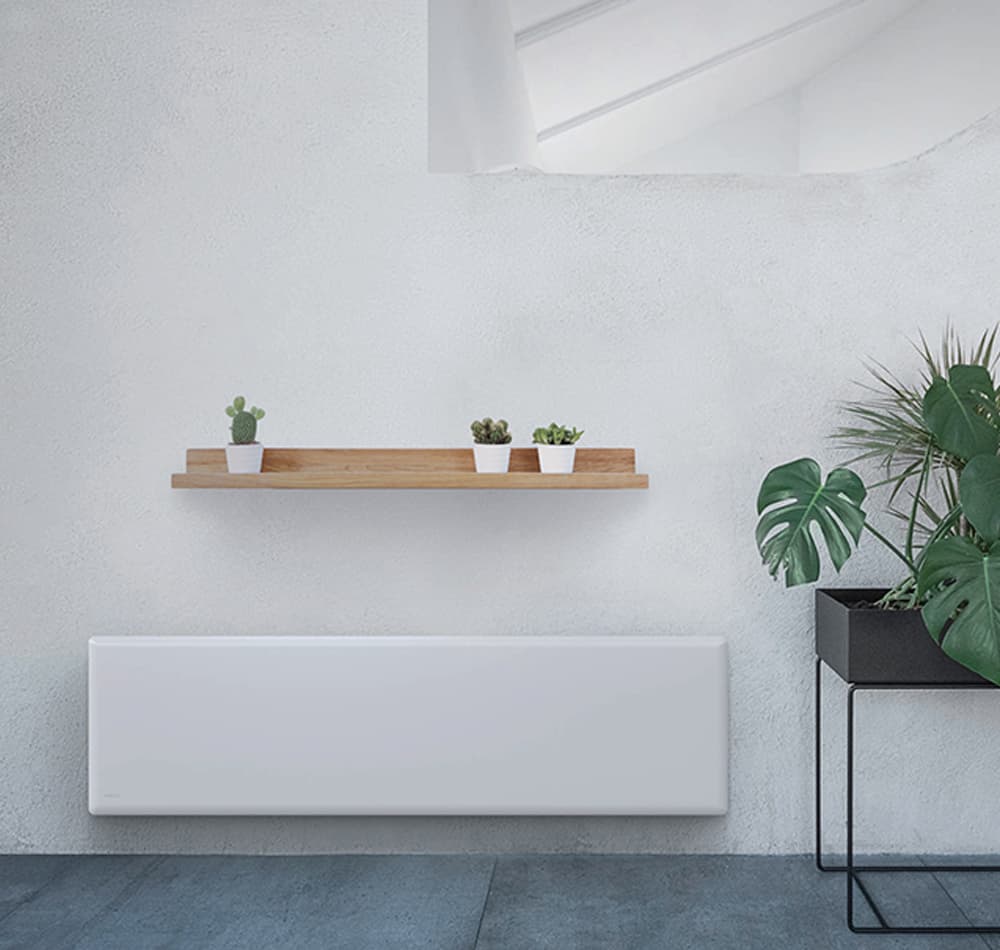 Stone tile floor and white wall with many green plants next to a slim long electric panel heater