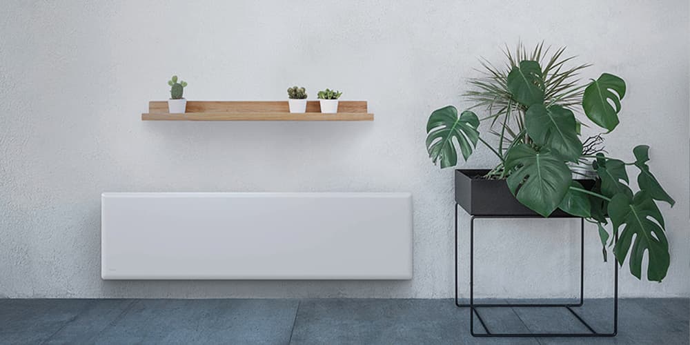 Stone tile floor and white wall with many green plants next to a slim long electric panel heater