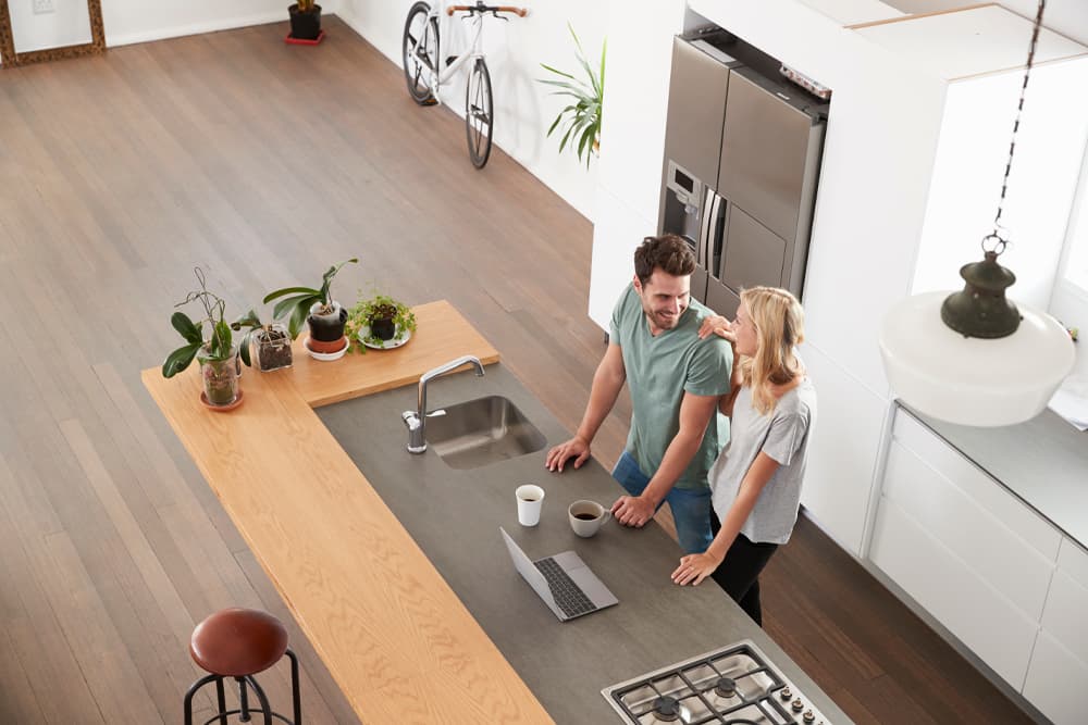 Happy couple standing in their newly renovated kitchen with a large stone benchtop and a raised wooden bar for dining