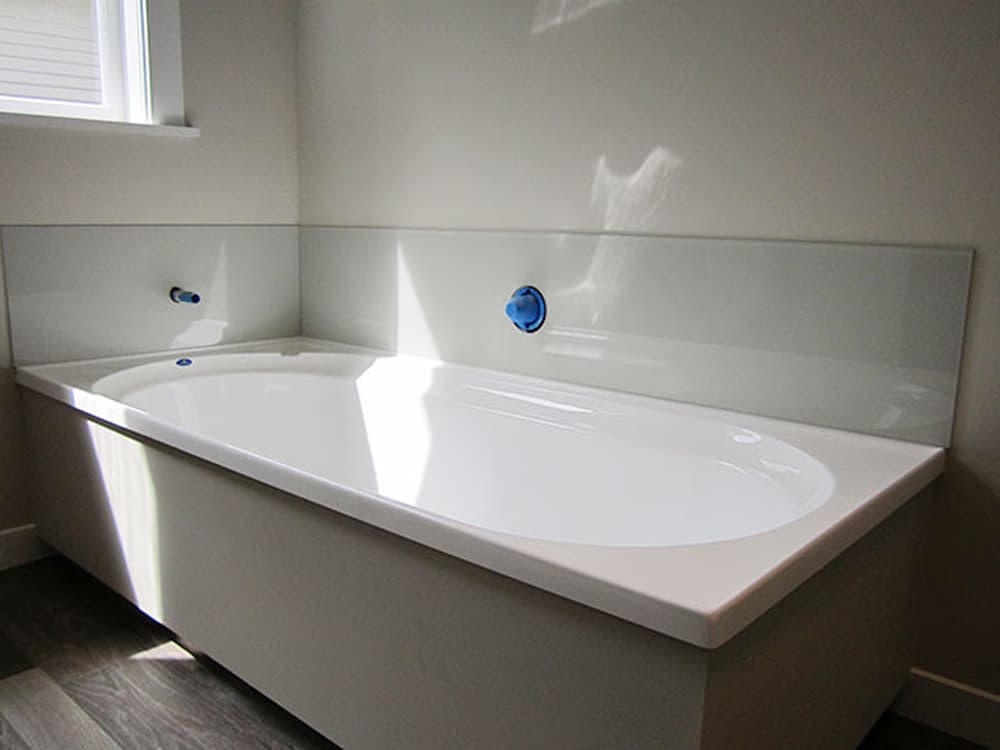 White bath tub with a grey splashback covering the immediate parts of the wall