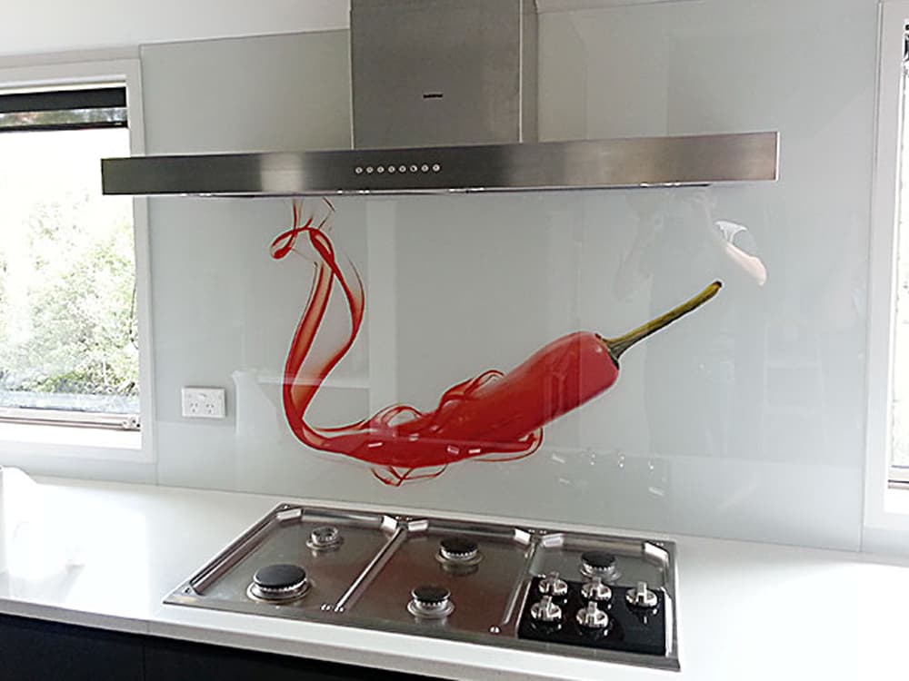 White kitchen with a large clear splashback with a smoking red chili under the rangehood 