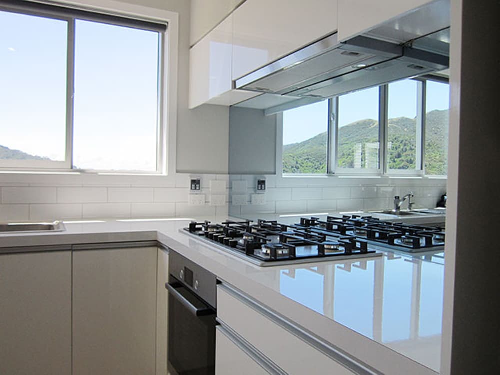 Classy white kitchen with a gas stovetop, white glossy benchtop, and a mirror splashback