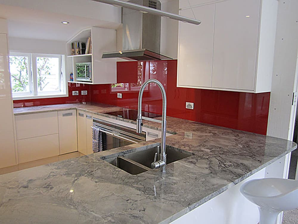 White marble kitchen benchtop with white cabinets and an outstanding glossy red splashback covering all of the walls above the bench in the kitchen