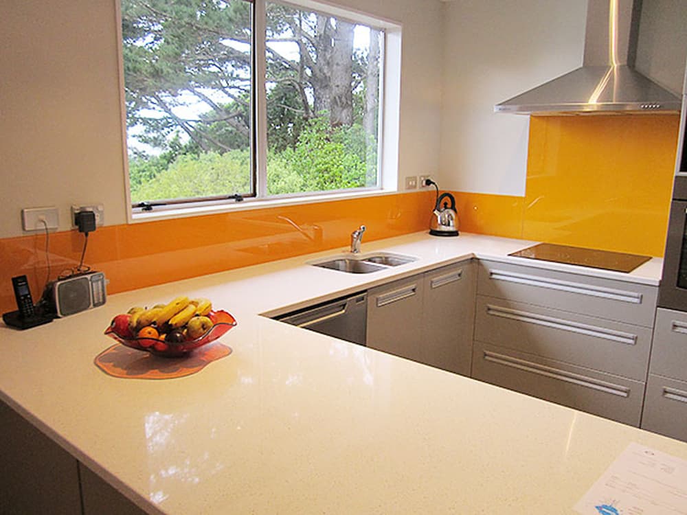 Prominent orange glossy splashback in a kitchen with a white shiny benchtop and grey cabinetry
