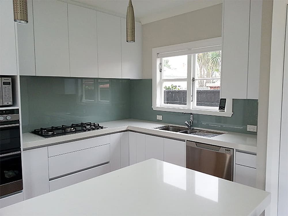 White kitchen cabinetry and benchtops with a reflective off-blue splashback and a large white kitchen island