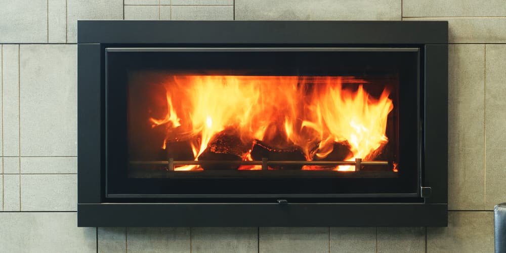 Beige stone tiled wall with an aluminum-framed built-in fireplace that displays fiery stones