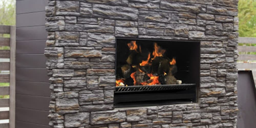 Outdoor fireplace that sits in rectangular weatherboard housing with a stone front and firewood stored below