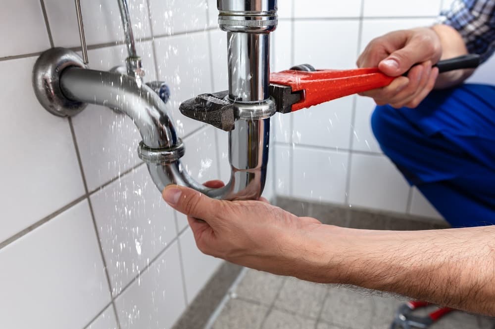 Gasfitter with bright orange gloves using a small wrench to tighten a pipe under a gas stove