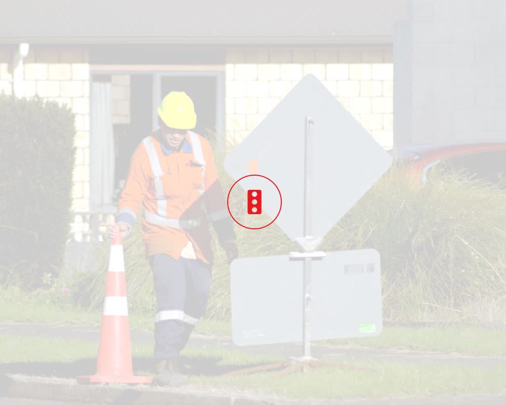 Traffic management worker in orange high viz reflective gear setting up a cone next to a roadworks sign on the side of the road