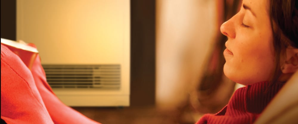 Warm yellow hue on a woman relaxing with her eyes shut sitting beside a gas heater
