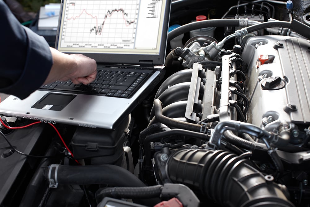 Motor Works Group specialised vehicle expert, using a laptop above the engine block