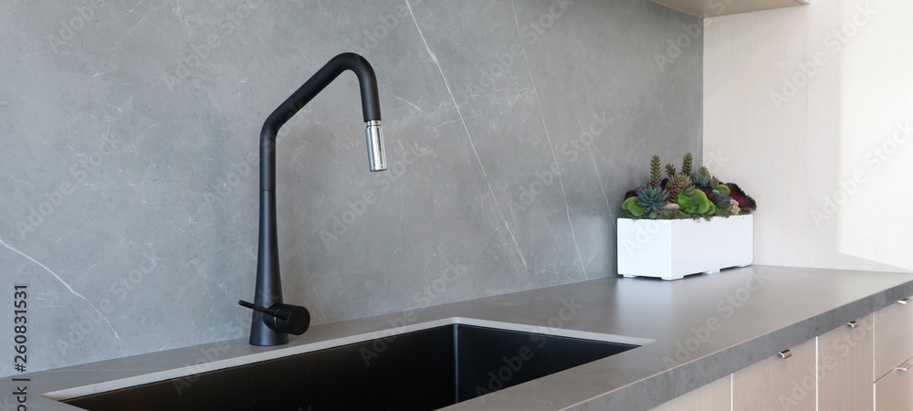 Grey quartz kitchen benchtop with a sleek black sink and tap and a white container with heaps of succulents