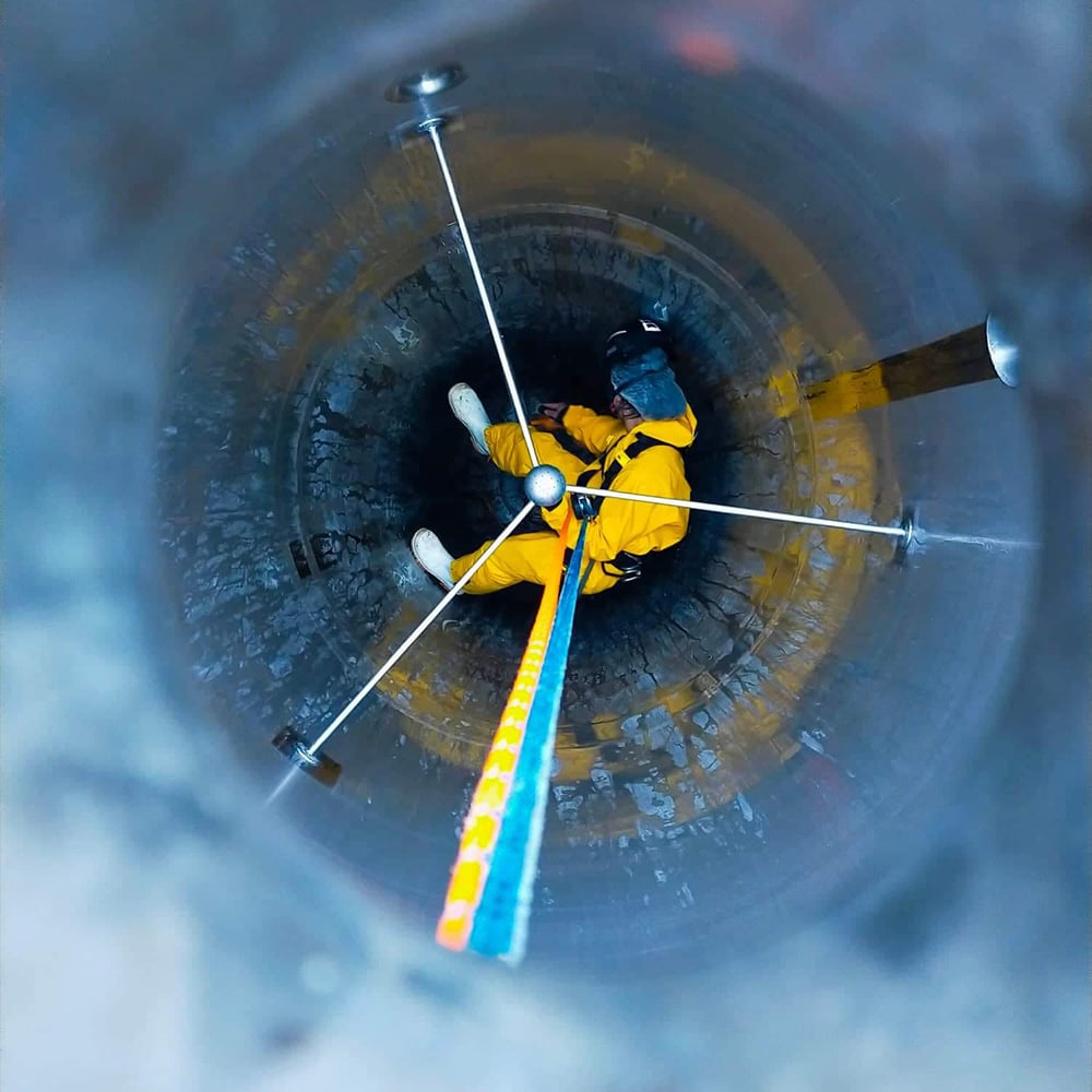Abseiler rappelled down inside a tank to clean the interior while in a yellow jumpsuit, a hairnet, and a safety mask 