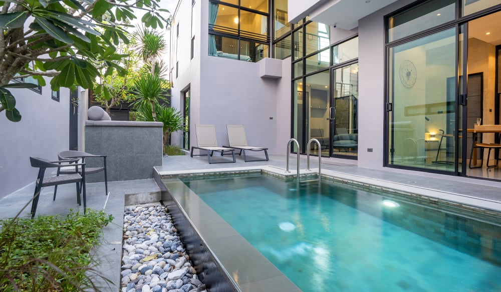 Modern white building with several outdoor accesses that lead to a stone tile backyard with a crystal clear pool