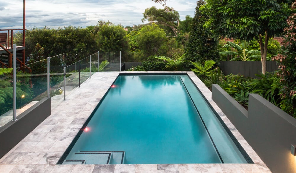 Minimalistic pool area design with a sleek glass fence and a fenceless pool area overlooking the garden