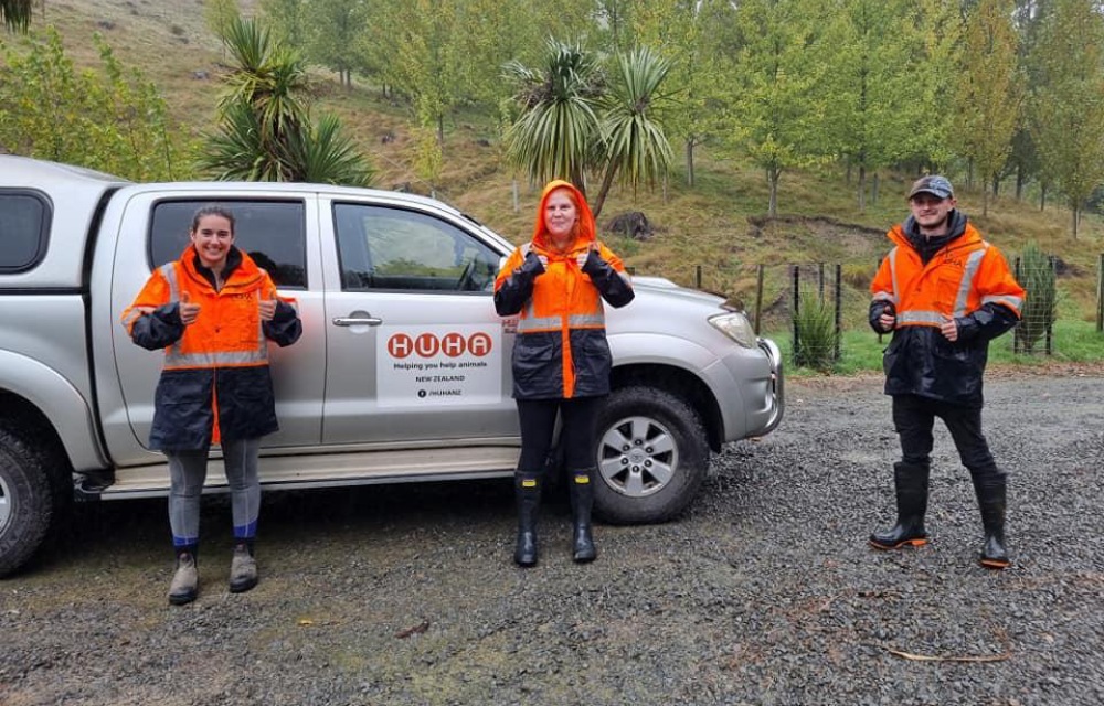 Three Huha team members in their wet weather orange high-viz jackets standing in front of a Huha branded ute
