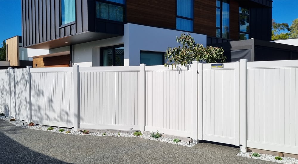 Modern white PVC fence with a textured concrete driveway in front of a modern container house