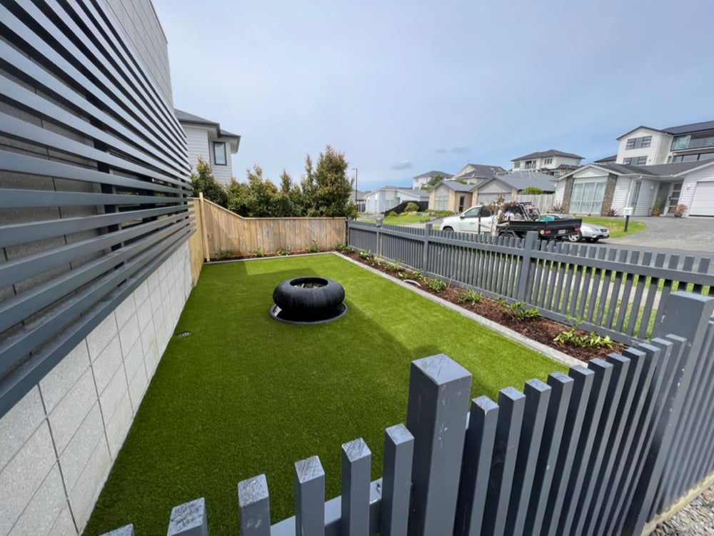 Well-groomed front lawn with a modern firepit and newly painted dark blue fence