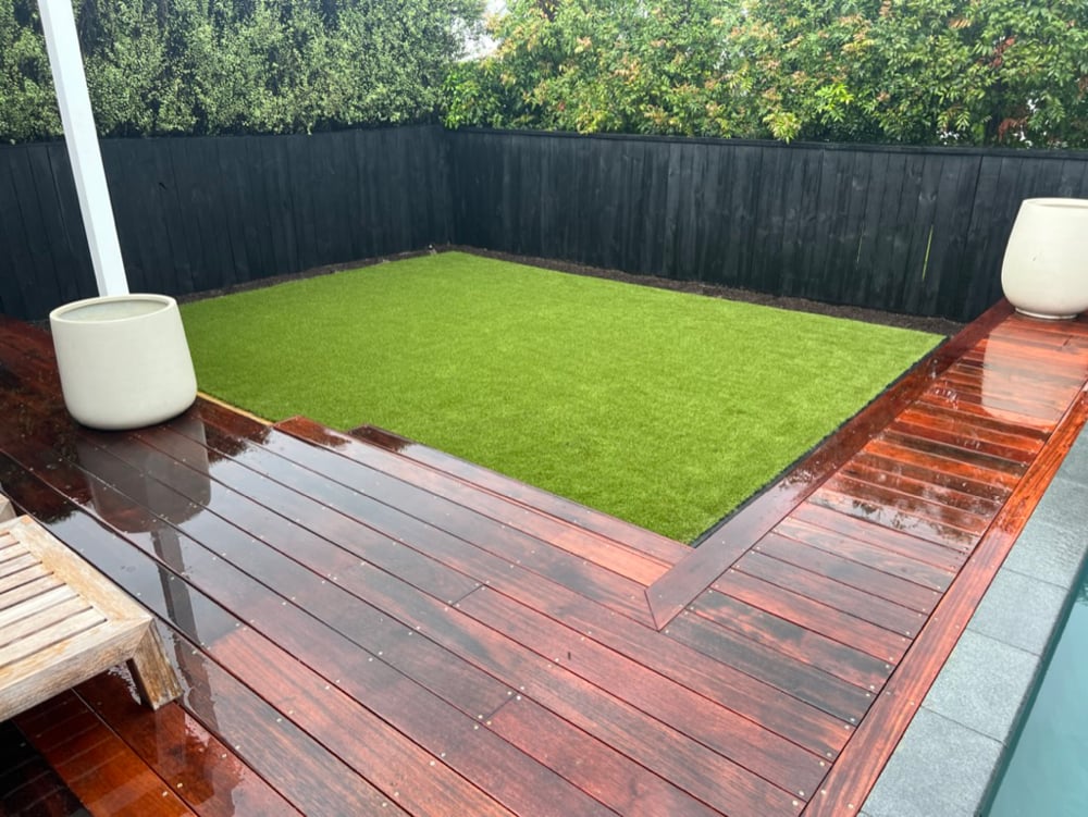 Recently water blasted deck with a perfectly mowed small lawn section and dark black painted fences with overarching trees