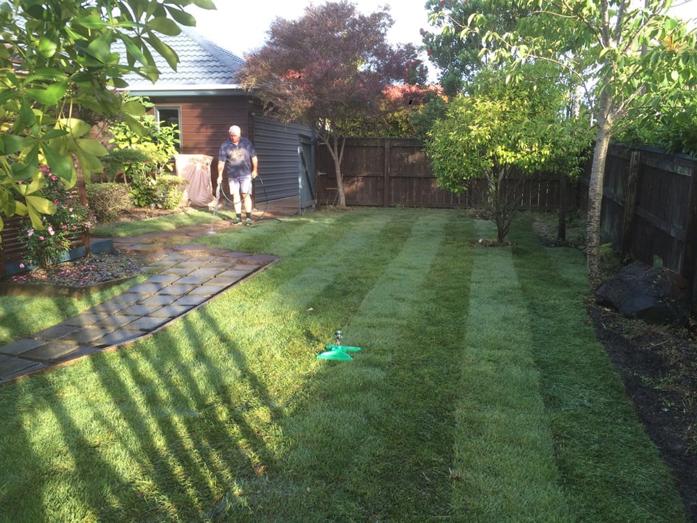 York Landscaping team member hosing down the stone brick path after mowing a nice striped pattern into the backyard grass