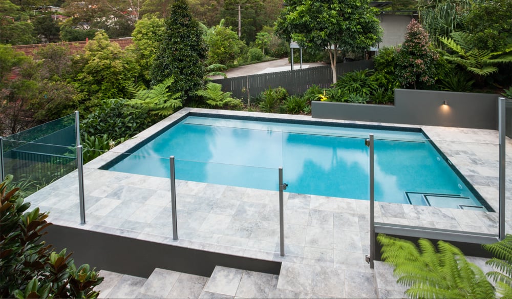 Minimalistic pool area design with a sleek glass fence and a fenceless pool area overlooking the garden