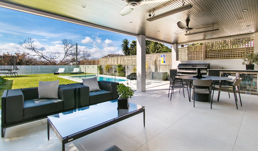 Massive outdoor area with a dining area and a couple outdoor lounging seats with a trampoline and a neat medium-sized pool in the background