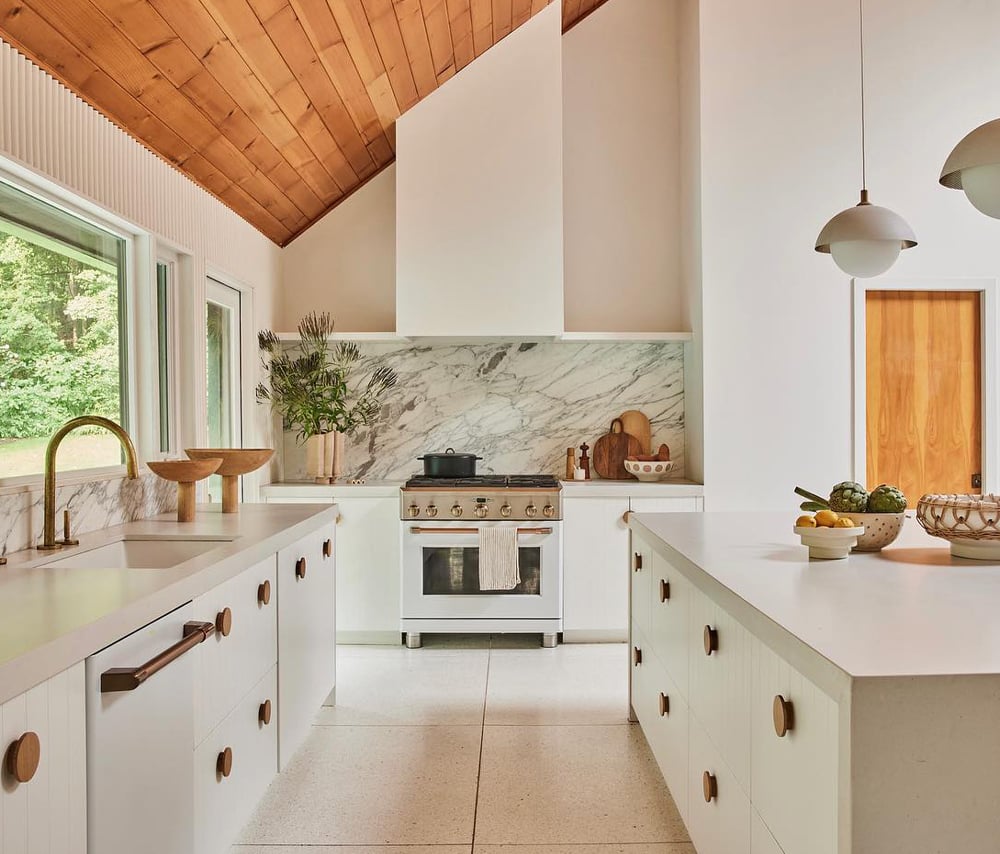 Minimalist white kitchen with brass fixtures and oak wood accents that create a sleek look