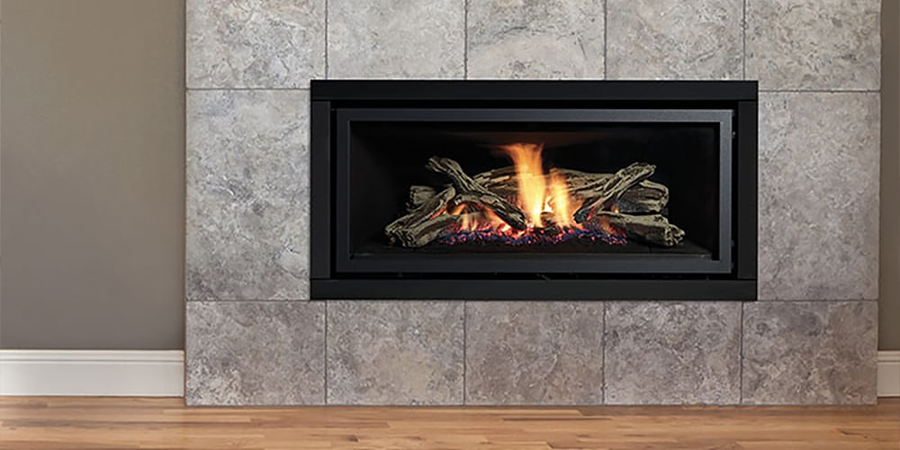 Lit black inbuilt gas fire with a stone tile frame in a room with grey walls and light wood floors