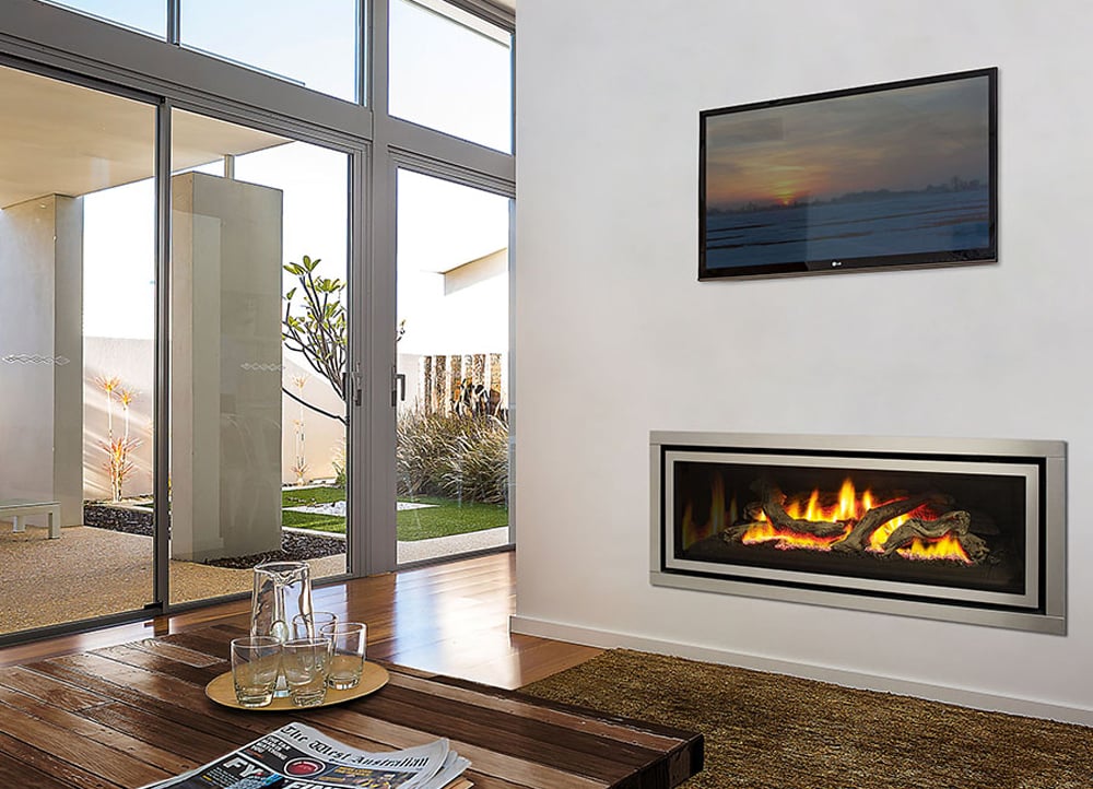 Hot gas fireplace built into the white wall under a TV with a cozy green rug under covering part of the shiny wooden floor