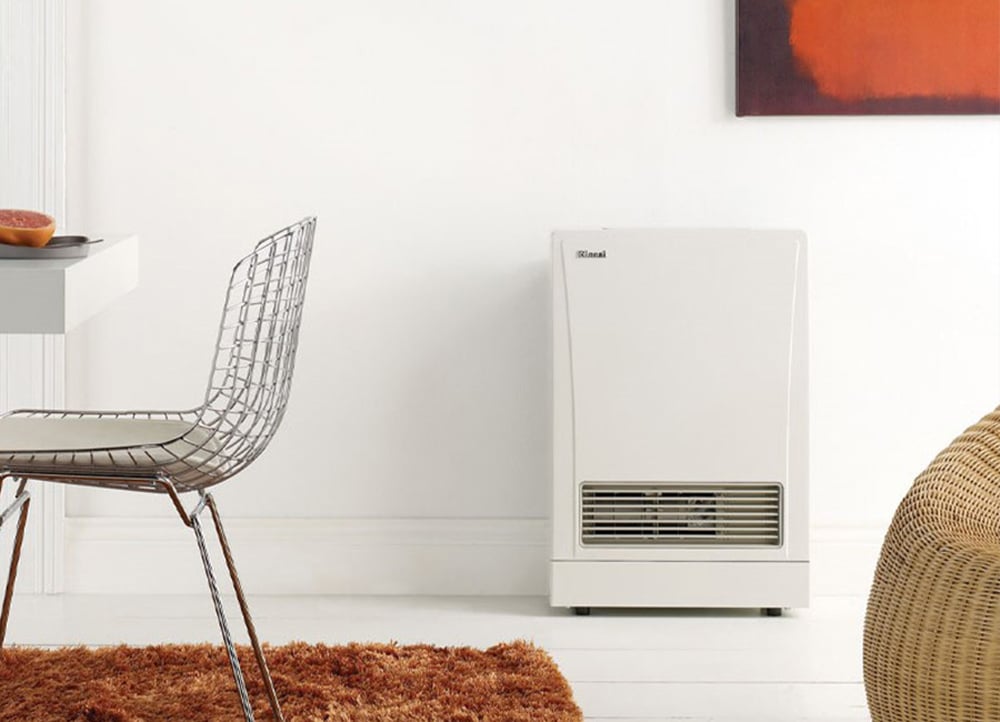 Simple white wall heater against a white wall next to a weaved basket and a metal net-like dining chair