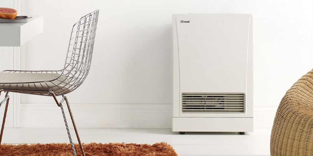 Simple white wall heater against a white wall next to a weaved basket and a metal net-like dining chair