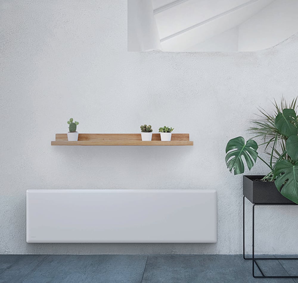 Stone tile floor and white wall with many green plants next to a slim long electric panel heater