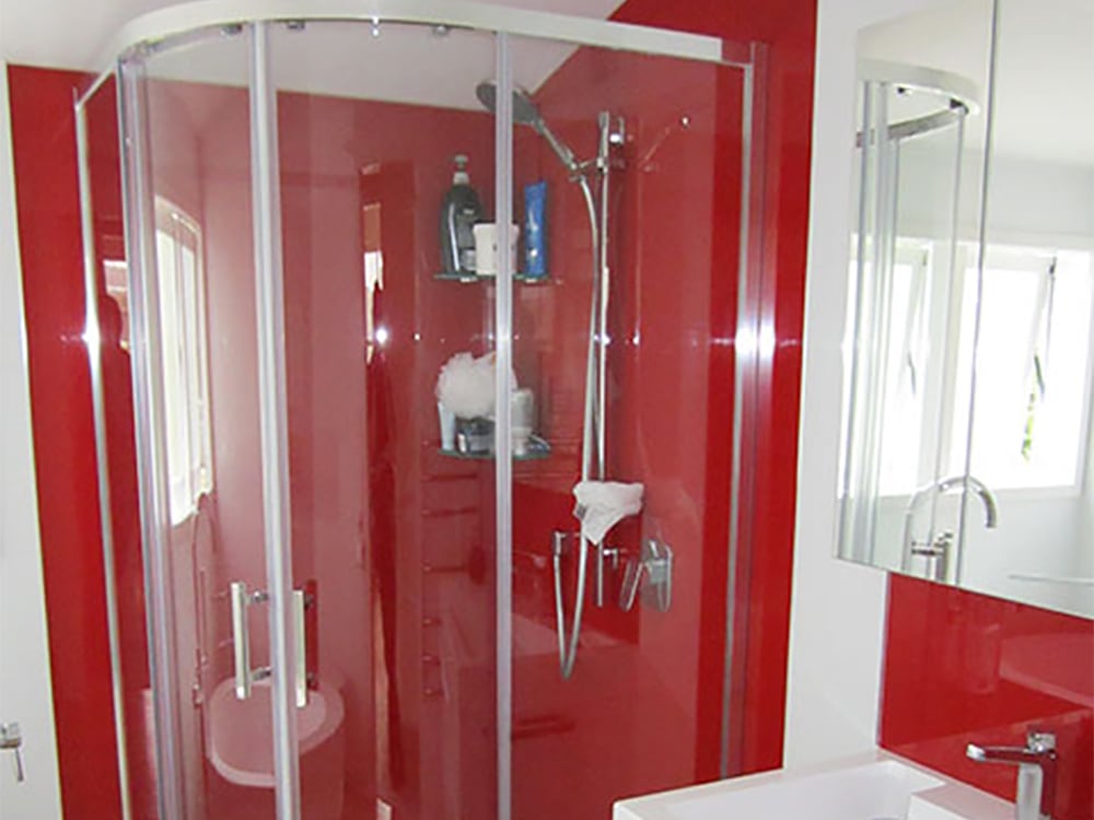 Large corner shower in a bathroom with white walls and a large red splashback that covers the shower wall and a bit above the sink