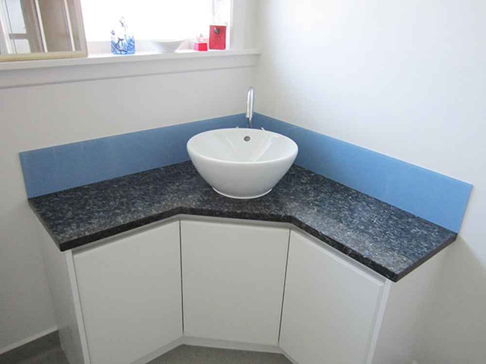 Small white sink on top of a bathroom basin with a granite countertop and a little blue splashback