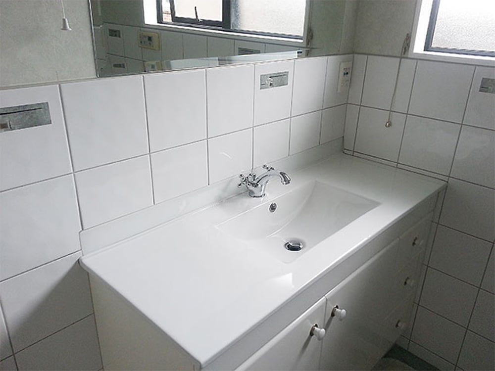Old white basin with an unbuilt sink and a large white tile splashback covering the wall up to below the mirror and window