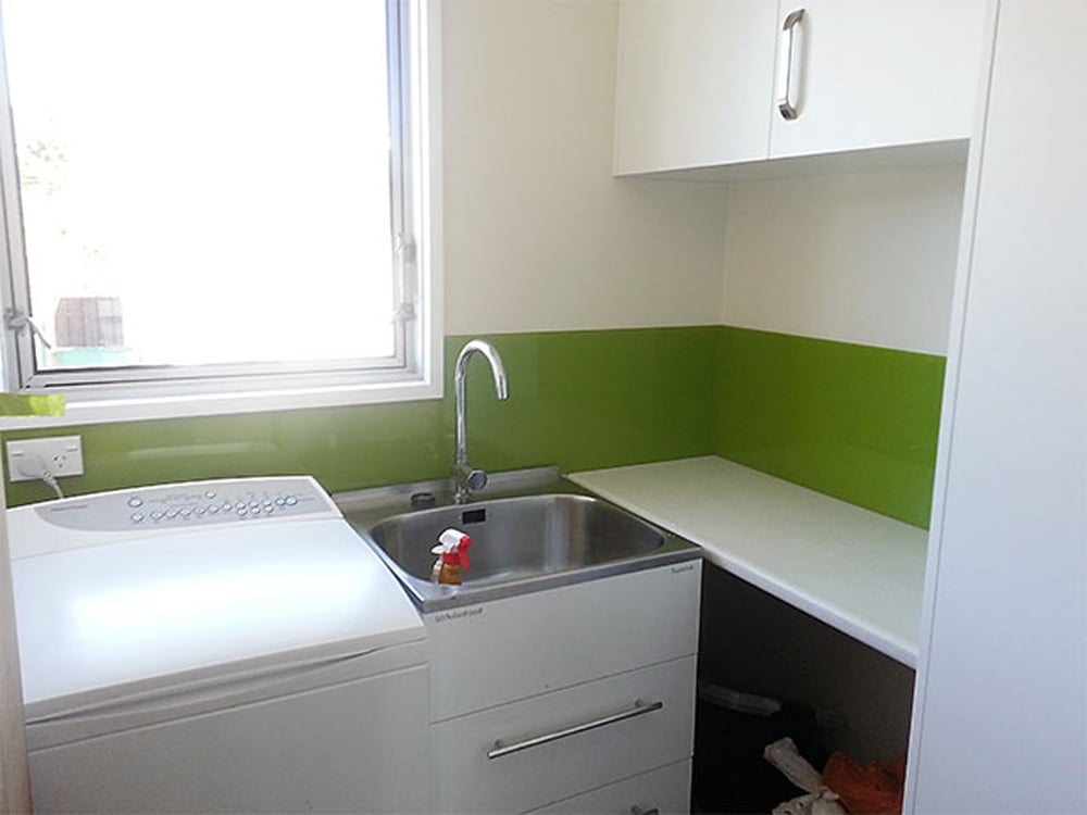 Small laundry corner with a washing machine, big silver sink and a low green splashback