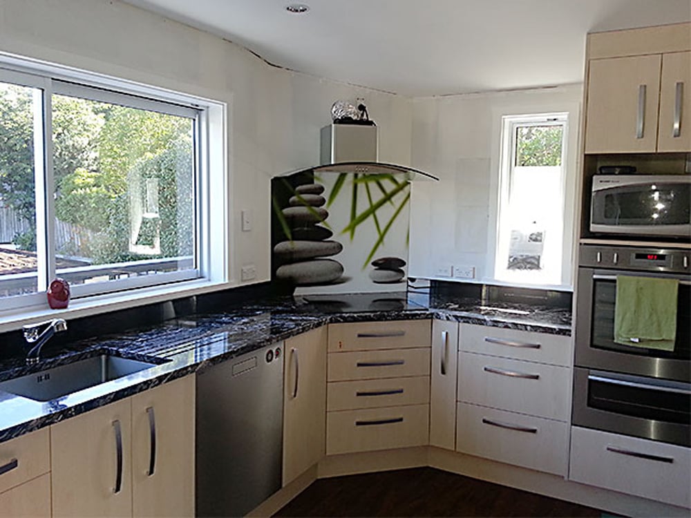 Tan coloured cabinetry and a black polished granite benchtop with a custom splashback on the wall with piled up rocks and green leaves on it
