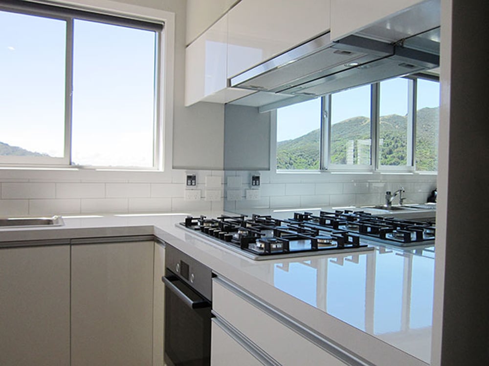 Classy white kitchen with a gas stovetop, white glossy benchtop, and a mirror splashback
