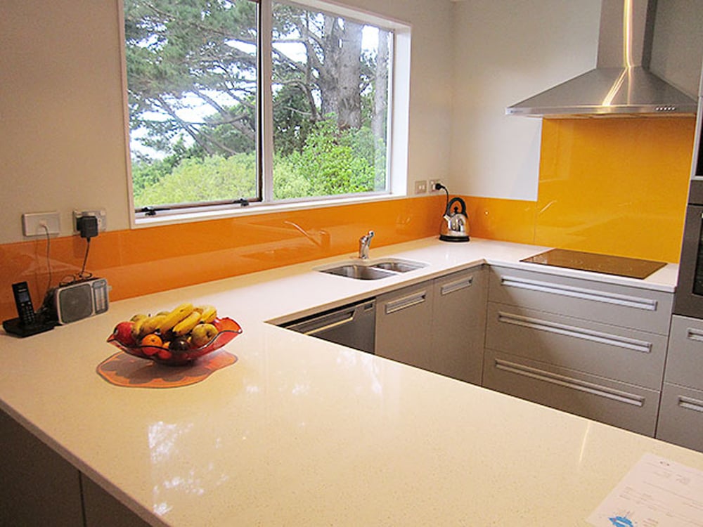 Prominent orange glossy splashback in a kitchen with a white shiny benchtop and grey cabinetry