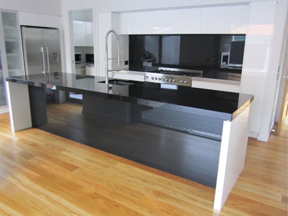 Light wood floors in a black and white kitchen with a glossy black splashback that contrasts with the surrounding white cabinets