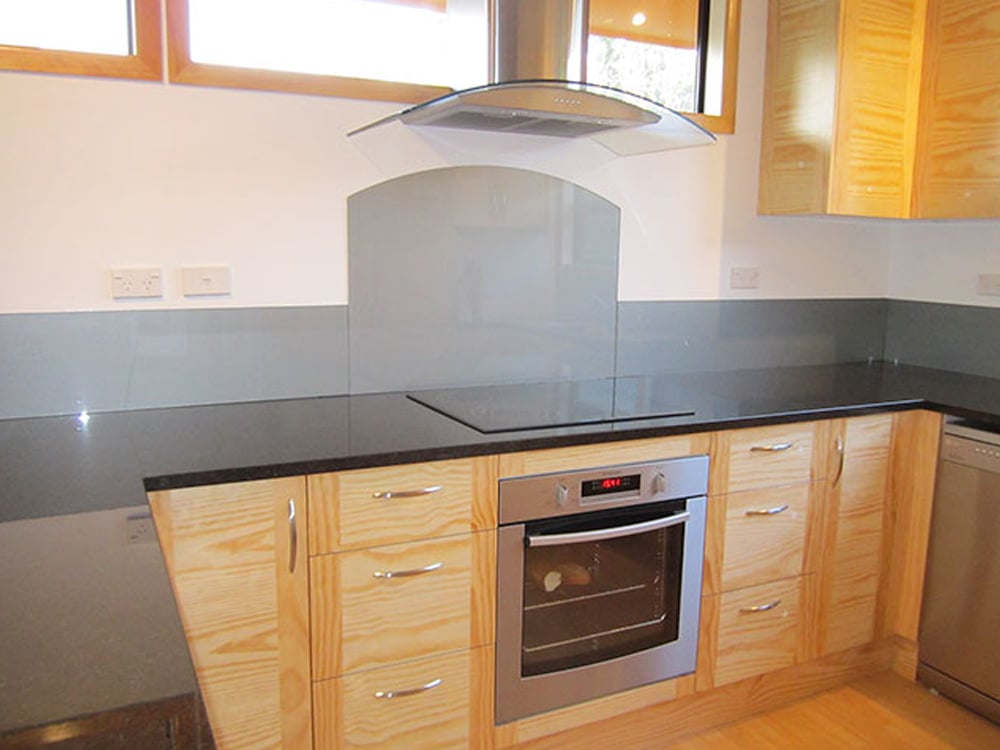 Oak kitchen cabinets with a sleek black benchtop and a grey custom cut splashback across the bottom of the wall