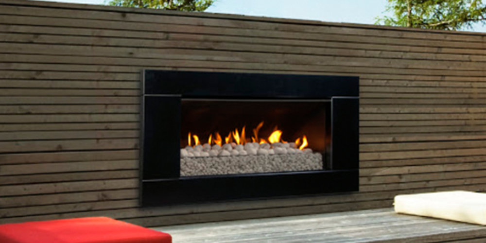 Black-framed gas fireplace built into an outdoor wooden wall next to sitting area with red and white cushions